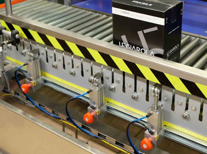 Carton handling through motorized rollers with manual adjustments of the spacers